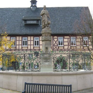 Ein Brunnen mit Fachwerkhaus im Hintergrund in der Altstadt von Königsberg in Bayern